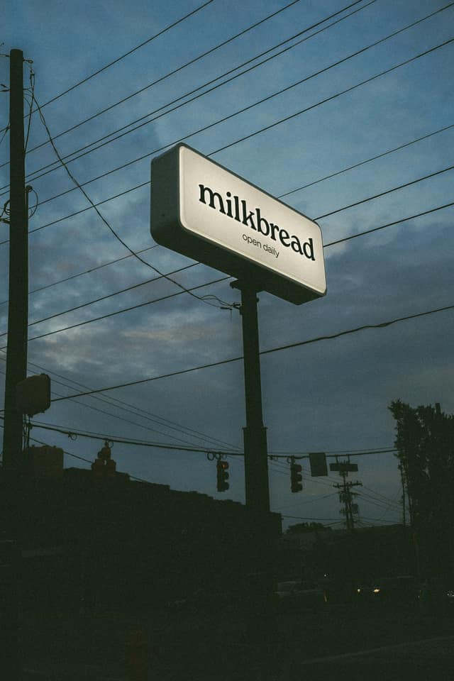 Milkbread’s illuminated roadside sign in Plaza Midwood at dusk.