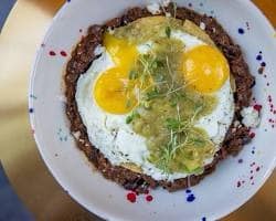 A breakfast plate topped with sunny-side-up eggs and green sauce at Uptown Yolk.