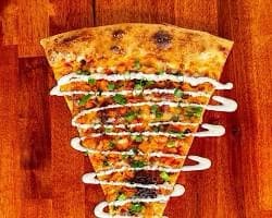 A large pizza slice with colorful toppings and drizzled sauce at Zämbies Pizza.