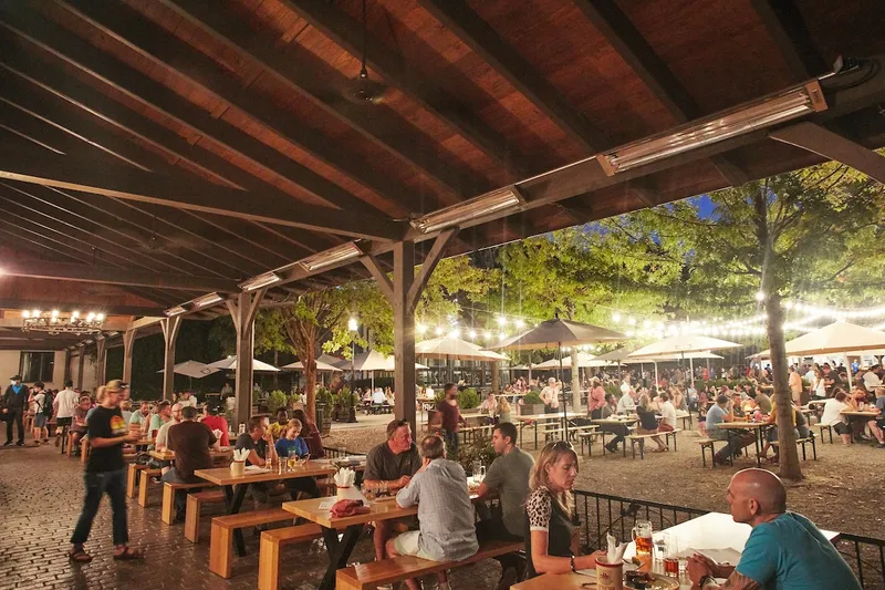 Guests at picnic tables beneath string lights in Olde Mecklenburg’s LoSo biergarten in Charlotte